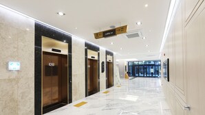 Un vestíbulo de hotel moderno con suelo de mármol, ascensores y una señalización clara.
