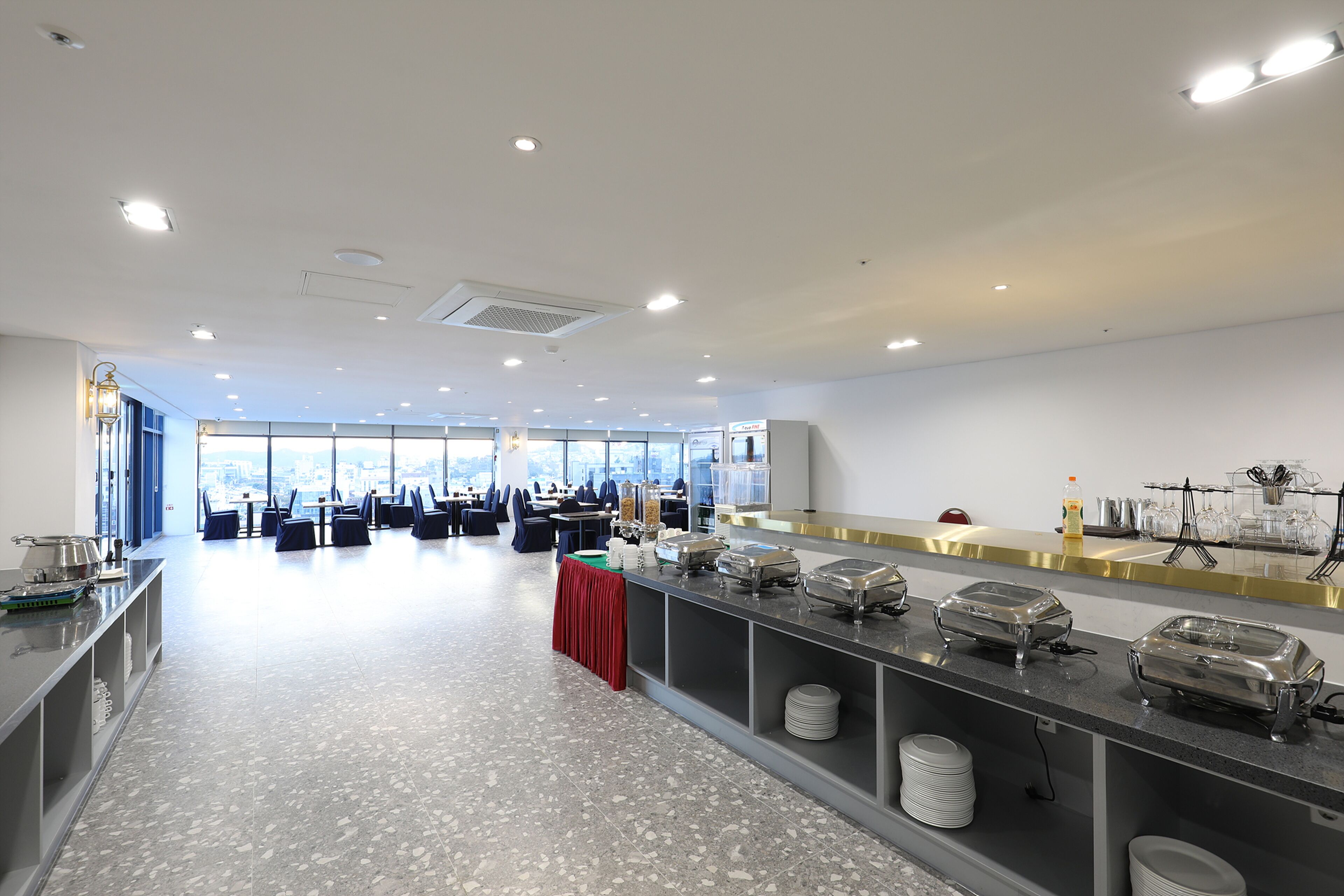 Een ruime kamer met een lange buffettafel, meerdere zithoeken en uitzicht door grote ramen.