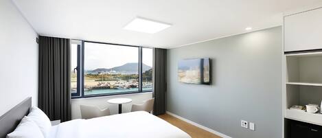 A hotel room with a bed, a small table, a chair, a TV, and a view of a marina.