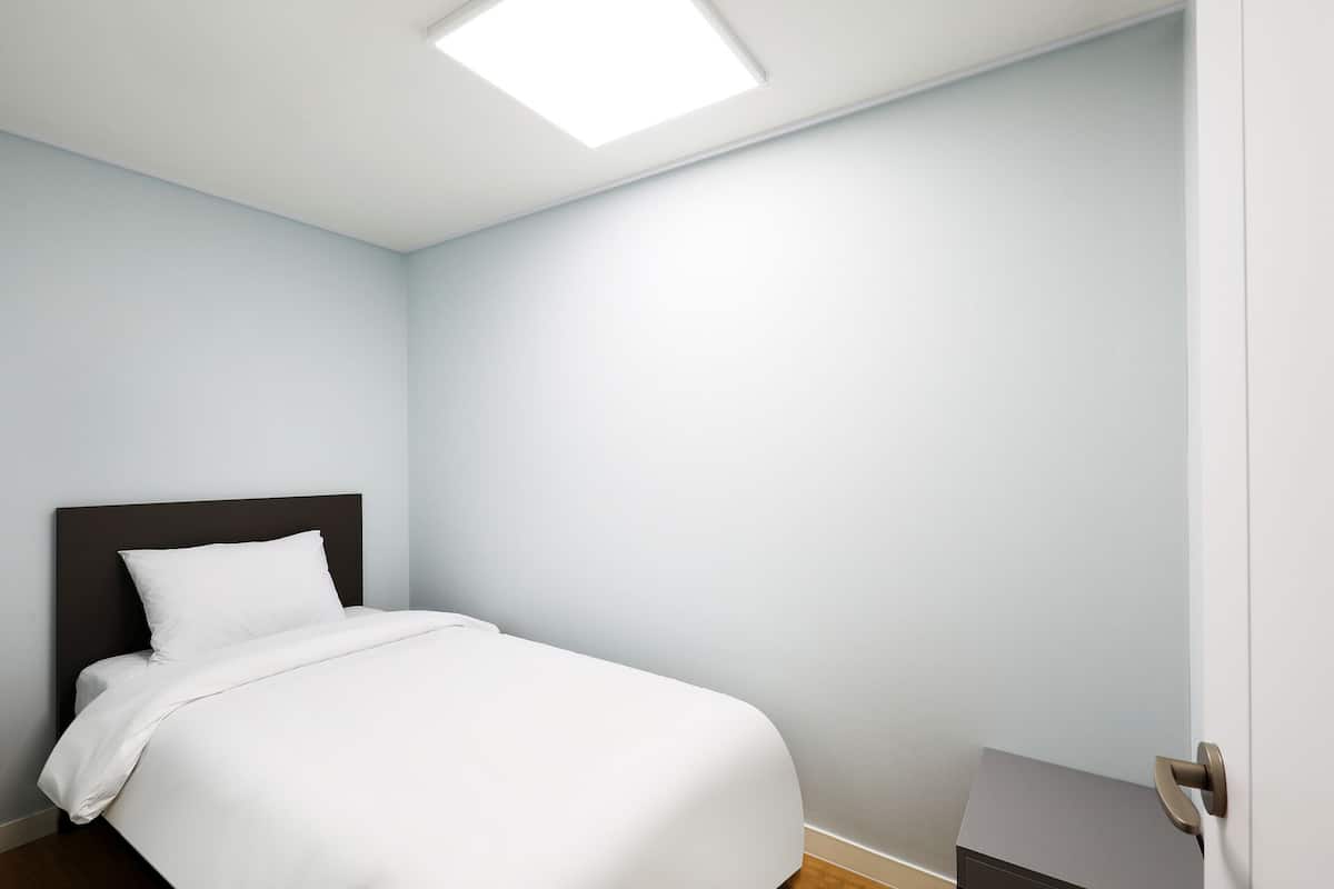 Una habitación de hotel con una cama, una puerta y una lámpara en el techo.