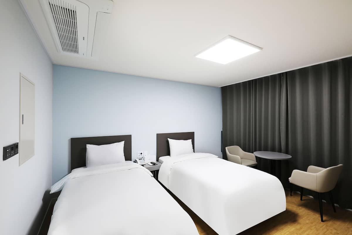 Habitación de hotel con dos camas, un escritorio, una silla, una mesita y una cortina.