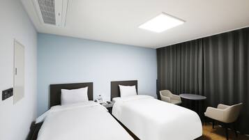 A hotel room with two beds, a desk, a chair, a small table, and a curtain.