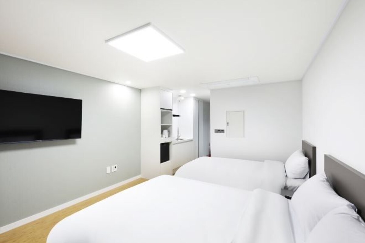 Une chambre d’hôtel moderne avec deux lits, un téléviseur à écran plat fixé au mur et une petite salle de bain.