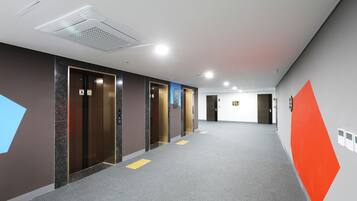 Un pasillo moderno con ascensores, pavimentos táctiles y señalización direccional.