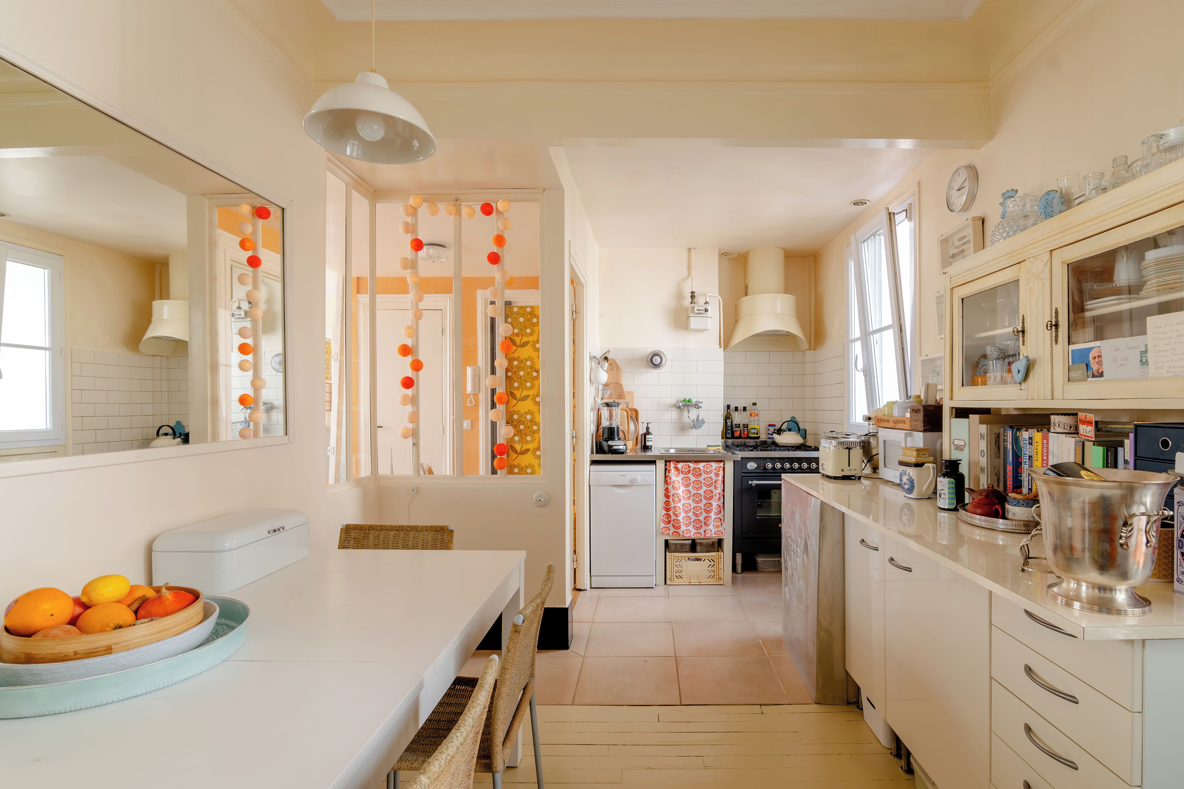 A kitchen with a white countertop, a dining table with a bowl of fruit, and a white refrigerator.