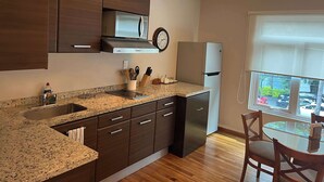 A modern kitchen with dark wooden cabinets, a stainless steel refrigerator, a microwave, and a sink. There is a dining area with a table and chairs, and a window with a view of the outside. - Arquimedes Deco - Colourful 1BR in Polanco (Mexico City)