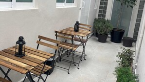 A patio area with wooden tables and benches, potted plants, and a building with large windows. - Arquimedes Deco - Colourful 1BR in Polanco (Mexico City)