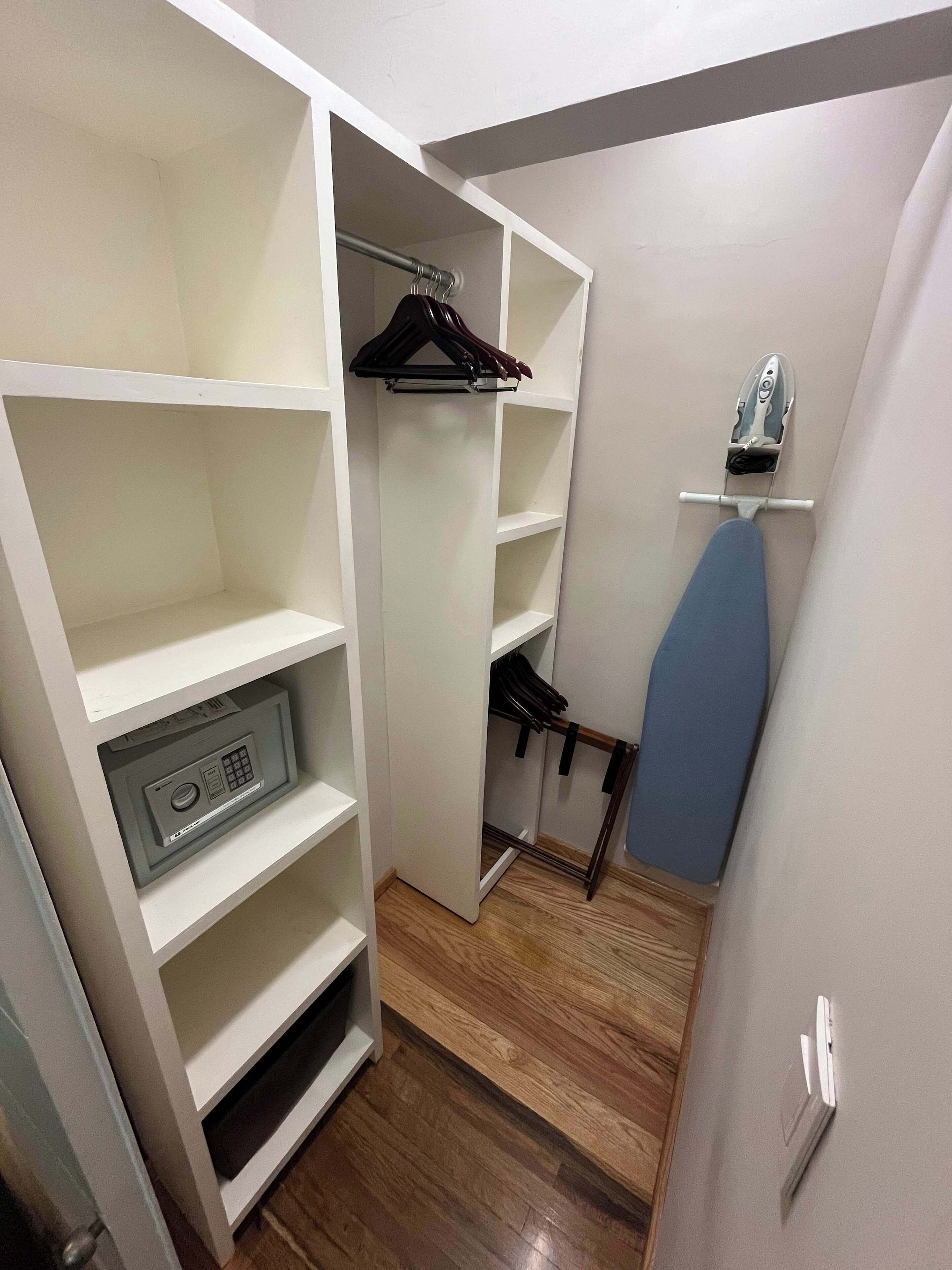 A walk-in closet with open shelving, a hanging rack, and a built-in ironing board.