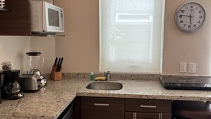 Eine Küche mit Granit-Arbeitsplatte, einer Mikrowelle, einem Spülbecken und einer Uhr an der Wand.