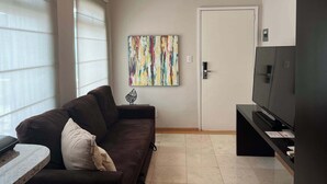 Ein Wohnzimmer mit einem braunen Sofa, einem Flachbildfernseher und einem farbenfrohen, abstrakten Gemälde an der Wand.