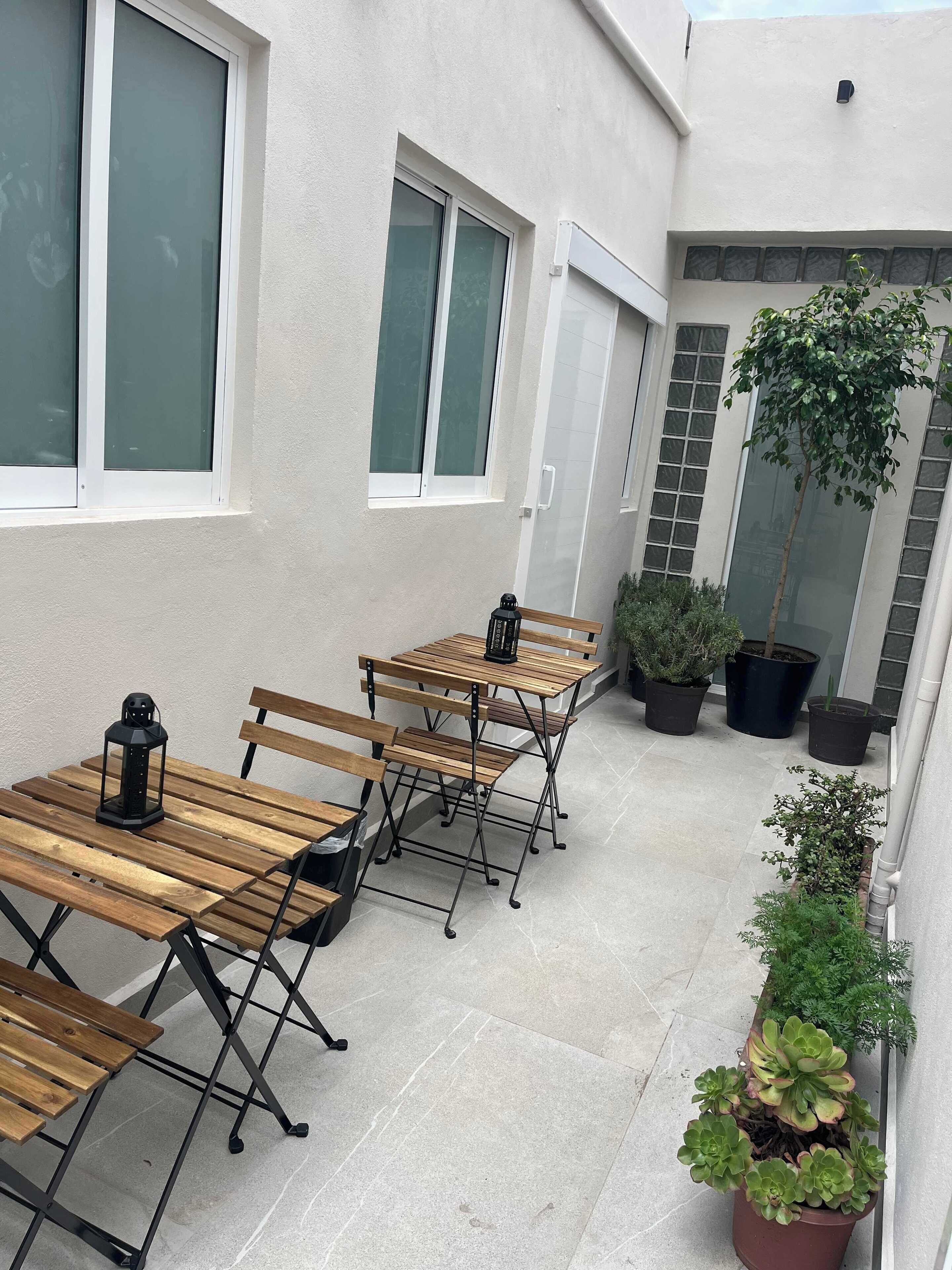 Un espace extérieur aménagé avec des tables et des bancs en bois, des plantes en pot et un bâtiment doté de grandes fenêtres.