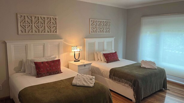 Quarto de hotel com duas camas, cada uma com cabeceira branca, mesa de cabeceira com abajur e arte decorativa na parede acima das camas.