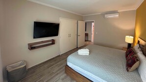 Une chambre d’hôtel avec un lit, un téléviseur fixé au mur, une table de chevet, une lampe et une porte donnant sur une autre pièce.