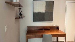 Une chambre moderne avec un bureau en bois, une chaise, une étagère murale agrémentée d’objets décoratifs et un tableau encadré.