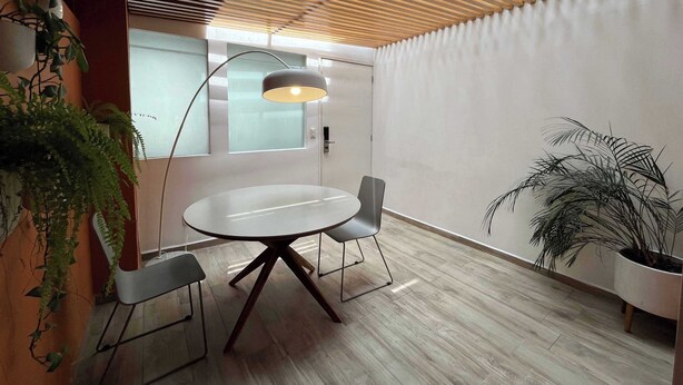 Une salle de réunion moderne avec une table ronde, deux chaises, un luminaire suspendu et des plantes en pot.