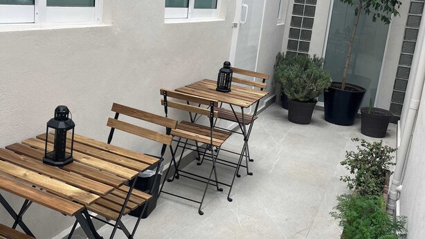 Ein Terrassenbereich mit Holztischen und -bänken, Kübelpflanzen und einem Gebäude mit großen Fenstern.