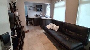 Ein Wohnzimmer mit einem dunkelbraunen Ledersofa, einem Fernseher und einer Küche im Hintergrund.
