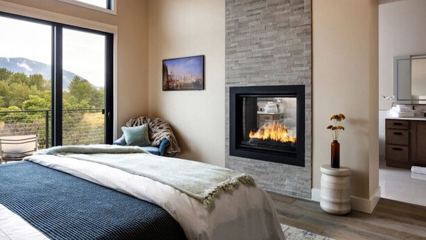 A modern bedroom with a large bed, a fireplace, and a view of the outdoors. - Summit + Sky (Bozeman)