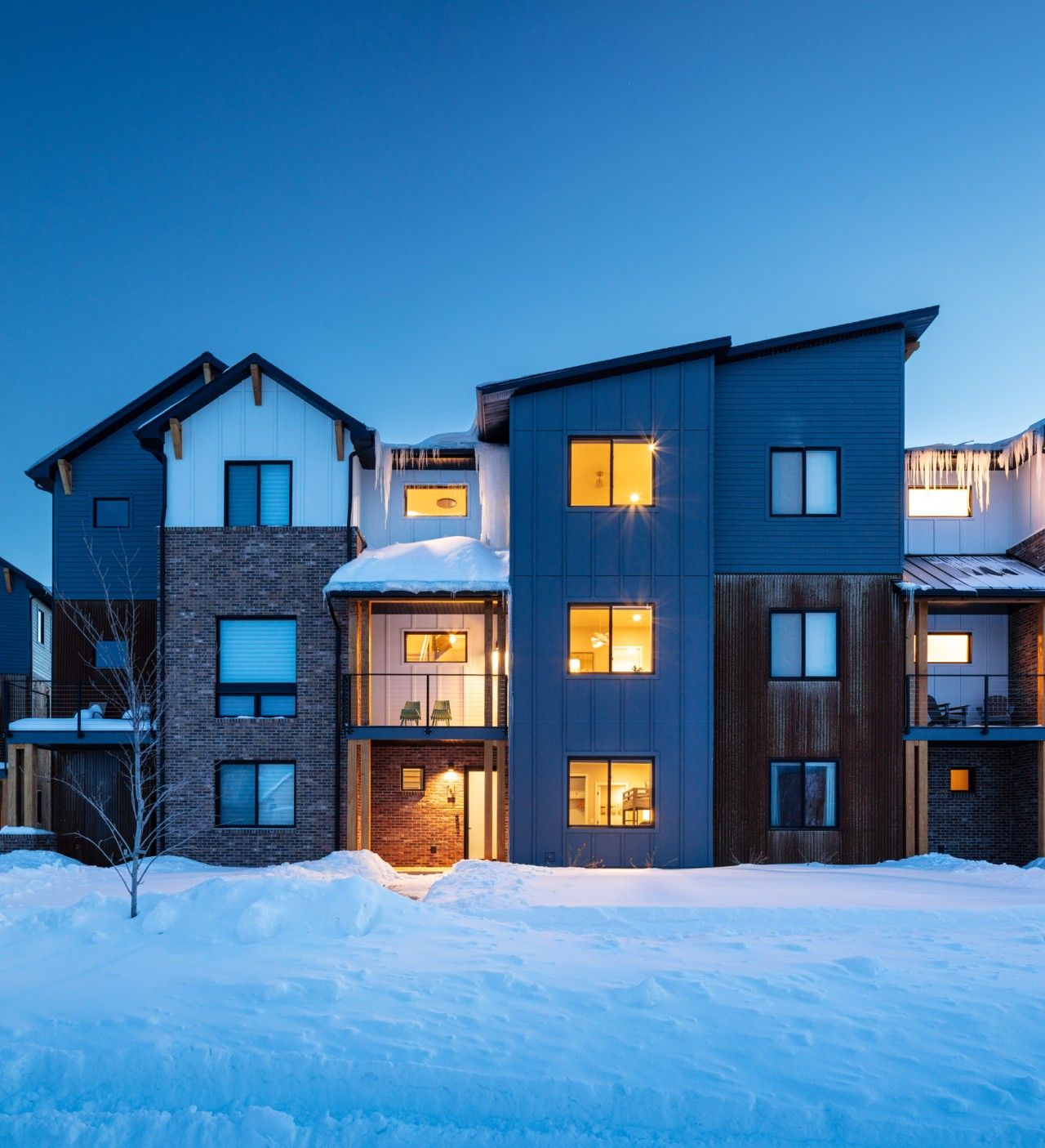 Un edificio residencial de varios pisos con fachada de ladrillo, ventanas grandes y un suelo cubierto de nieve.