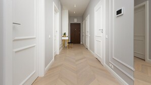 A hallway with white doors, a small table with a plant, and a wooden floor. - Spacious Apartment with Balcony | Parking | Gym (Warszawa)