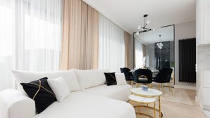 A modern living room with a white sectional sofa, a small round table, and black and gold chairs. - Spacious Apartment with Balcony | Parking | Gym (Warszawa)