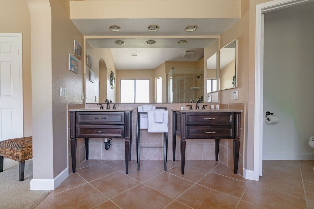 Une salle de bain avec deux lavabos, un banc et un grand miroir.