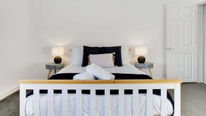 A bedroom with a white crib, a bed with white bedding, two bedside tables with lamps, and a white door. - Family two Bedroom Home Free Parking and Backyard (Howden-le-Wear)