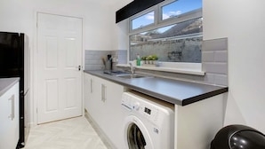 A compact kitchen with a washing machine, a sink, and a window overlooking a residential area. - Family two Bedroom Home Free Parking and Backyard (Howden-le-Wear)