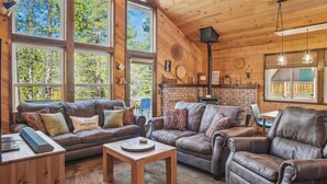 A cozy living room with leather sofas, a coffee table, and large windows offering a view of the outdoors.