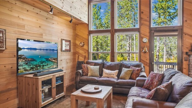 A cozy cabin interior with a wooden interior, a leather sofa, a wooden coffee table, and a television on a wooden cabinet.
