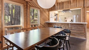 A wooden interior with a large dining table, chairs, and a kitchen area with a modern design.
