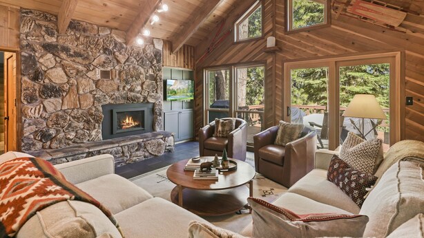 A cozy living room with a stone fireplace, leather sofas, and large windows offering a view of the outdoors.