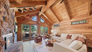 A cozy log cabin interior with a fireplace, comfortable seating, and large windows offering views of the outdoors.