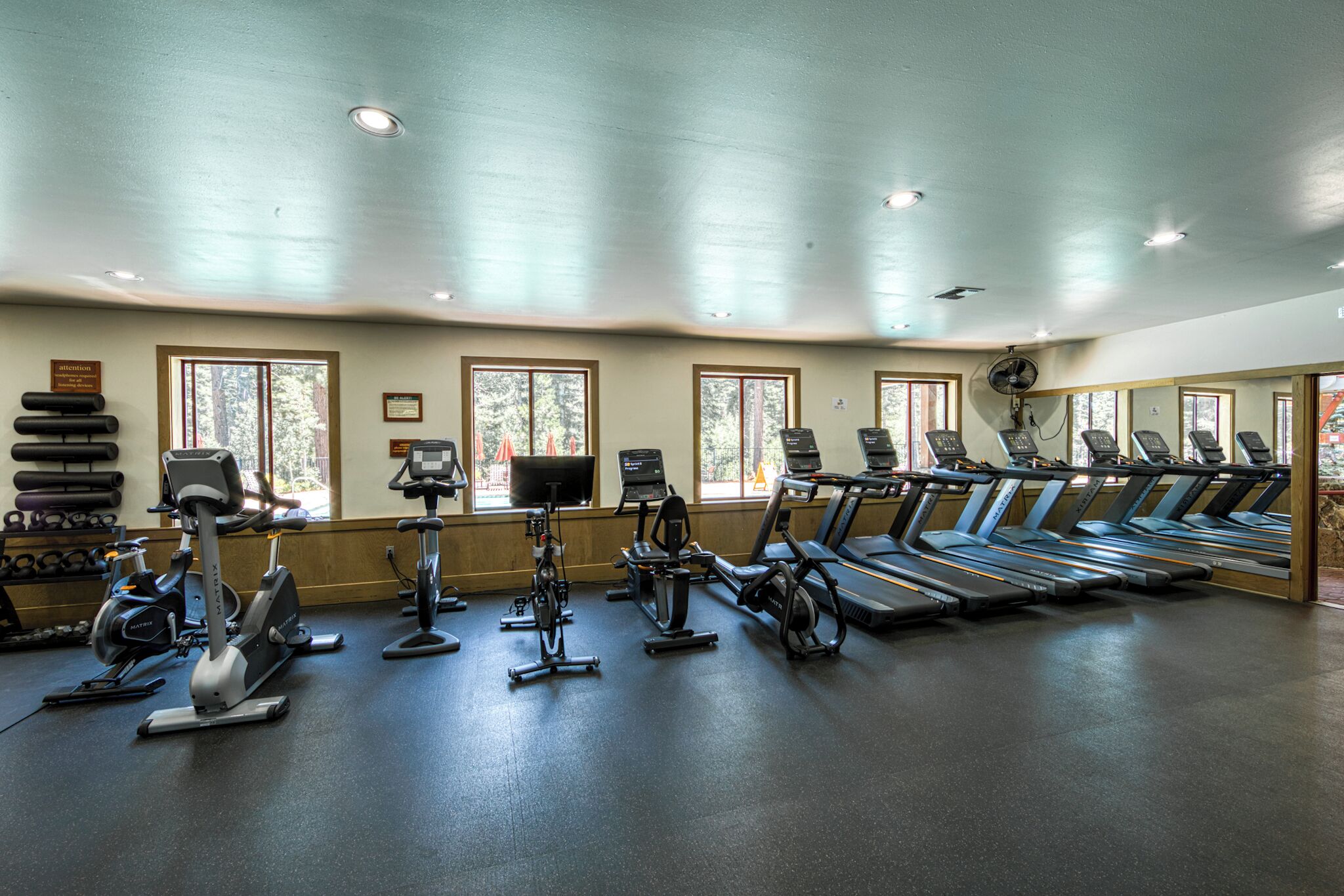 A gym with various exercise equipment, large windows, and a ceiling fan.