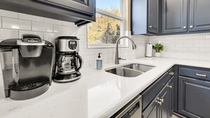 A modern kitchen with dark cabinets, a coffee maker, a coffee pot, and a sink. - 5BR Retreat Sleeps 16 | Hot Tub, Game Room (Hollister)
