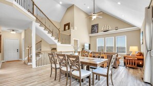 A spacious living area with a high ceiling, a staircase, a dining table with chairs, and a cozy seating area with a sofa and a lamp. - 5BR Retreat Sleeps 16 | Hot Tub, Game Room (Hollister)