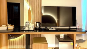Quarto de hotel moderno com parede de painel de madeira, TV de tela plana, cafeteira e mini-geladeira.