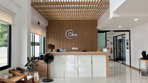 Uma área de recepção moderna com um balcão de madeira, um ventilador e um espaço de estar com cadeiras e uma mesa.