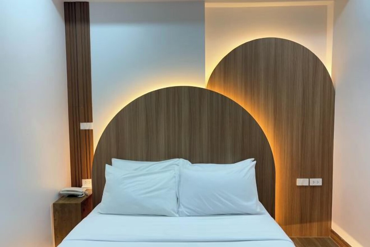 A modern hotel room with a large bed, wooden headboard, and a nightstand with a phone.