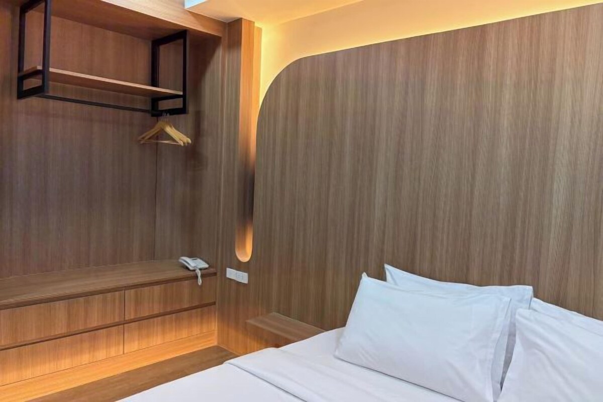 A modern hotel room with a wooden headboard, a bedside table with a phone, and a hanging coat rack.