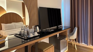 Quarto de hotel com uma cama, uma escrivaninha, uma televisão de tela plana, um mini-refrigerador e uma cadeira.