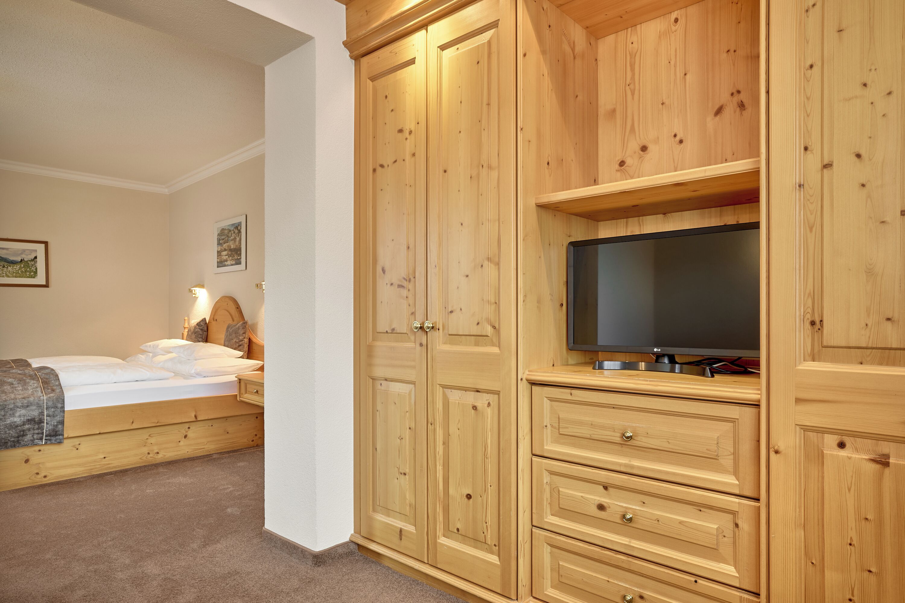A bedroom with a bed, wooden wardrobe, and a television.