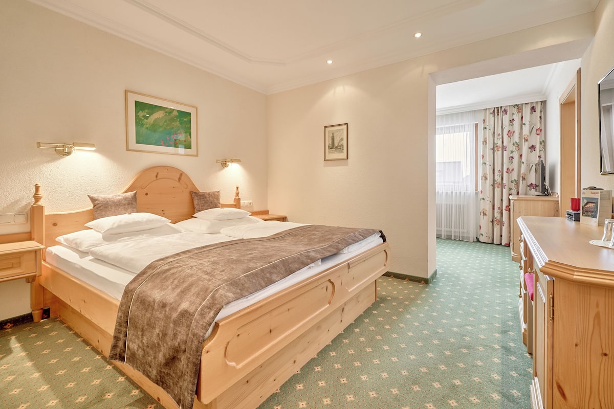 A hotel room with a wooden bed, two bedside tables, a dresser, and a mirror.