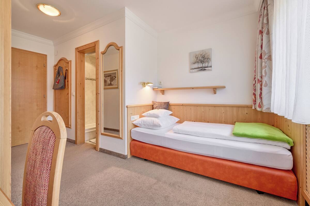 A bedroom with a wooden bed, a mirror, a shelf with a picture, and a door.