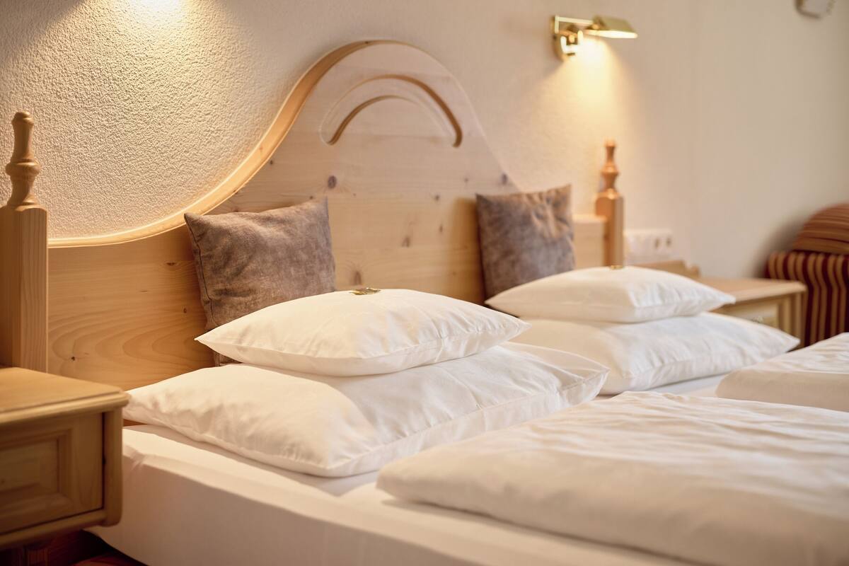 A neatly made bed with white linens and pillows, a wooden headboard, and a bedside table with a lamp.