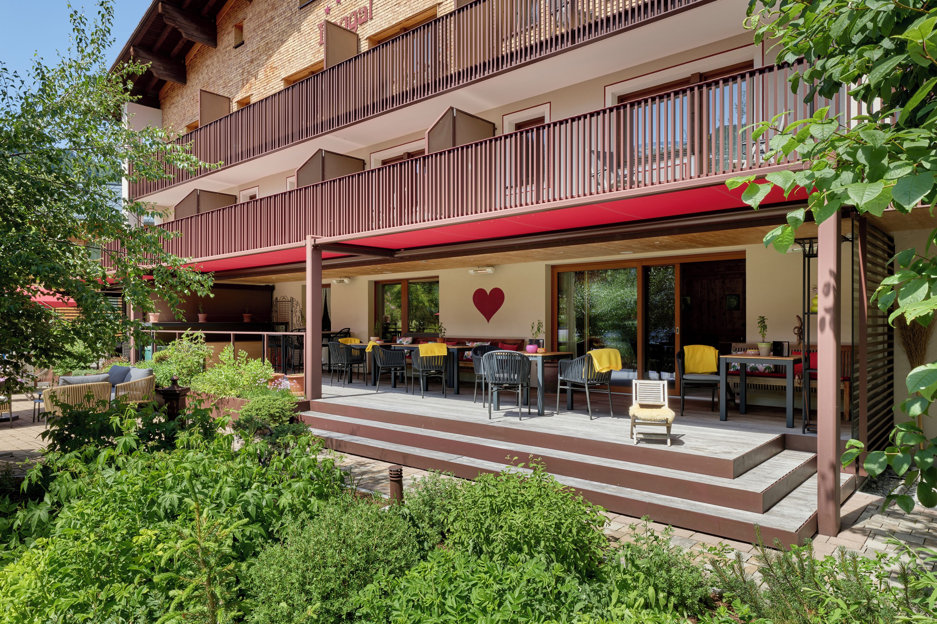 A two-story building with a covered outdoor seating area, a heart-shaped decoration on the wall, and steps leading to the entrance.
