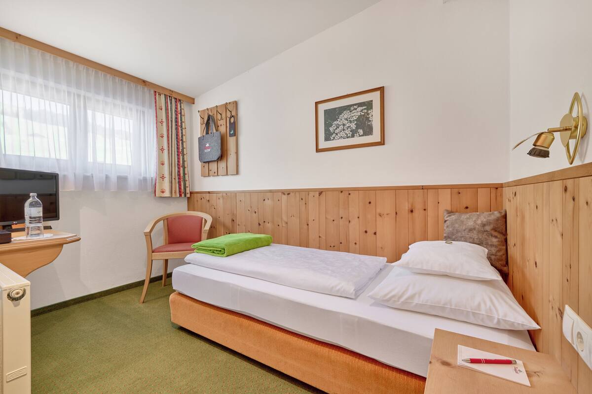 A hotel room with a bed, a chair, a desk, a television, and a wall-mounted lamp.