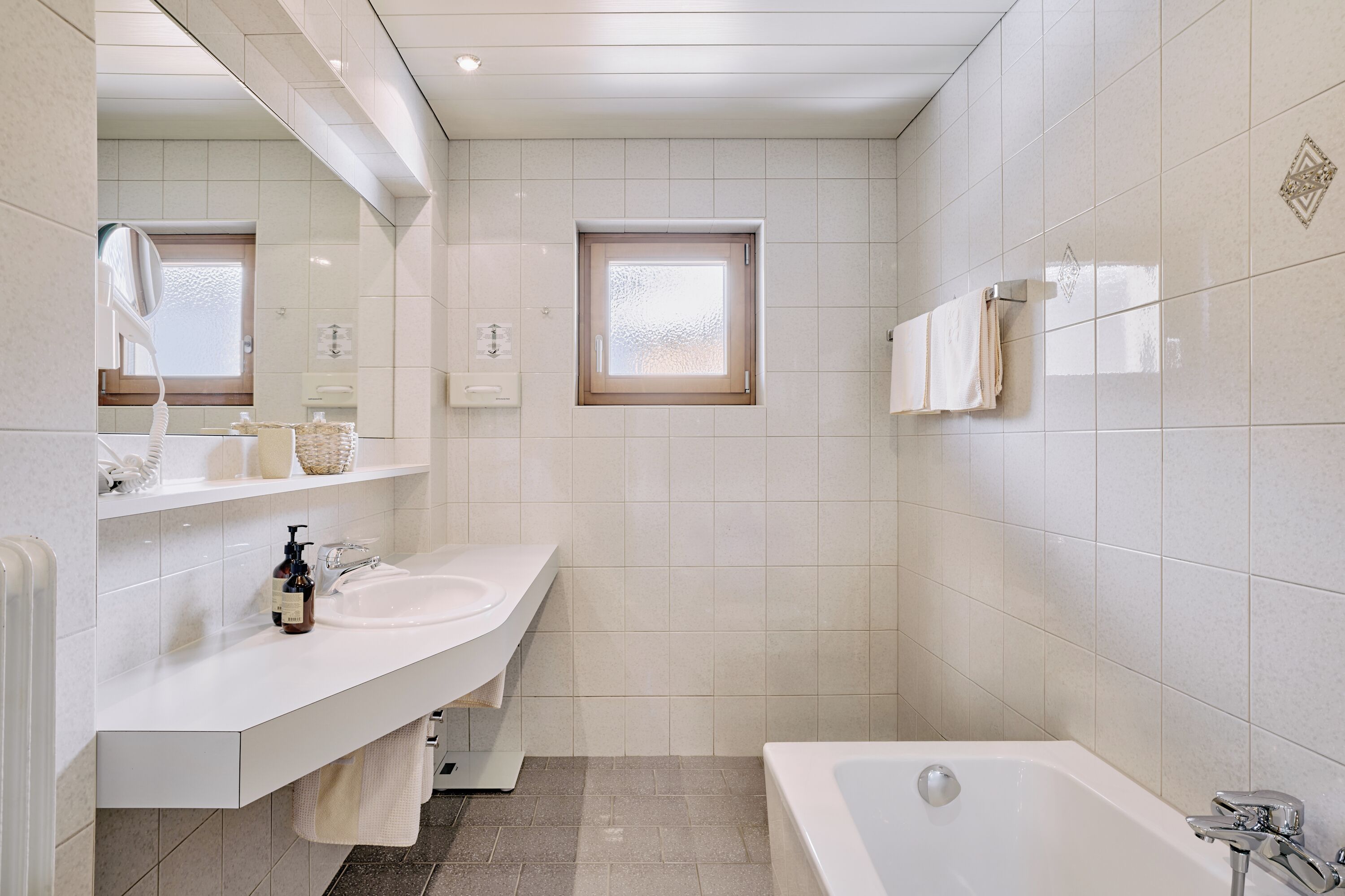 Une salle de bain moderne avec un lavabo blanc, un meuble-lavabo et une baignoire. Il y a une fenêtre au-dessus du lavabo et un porte-serviettes au mur.