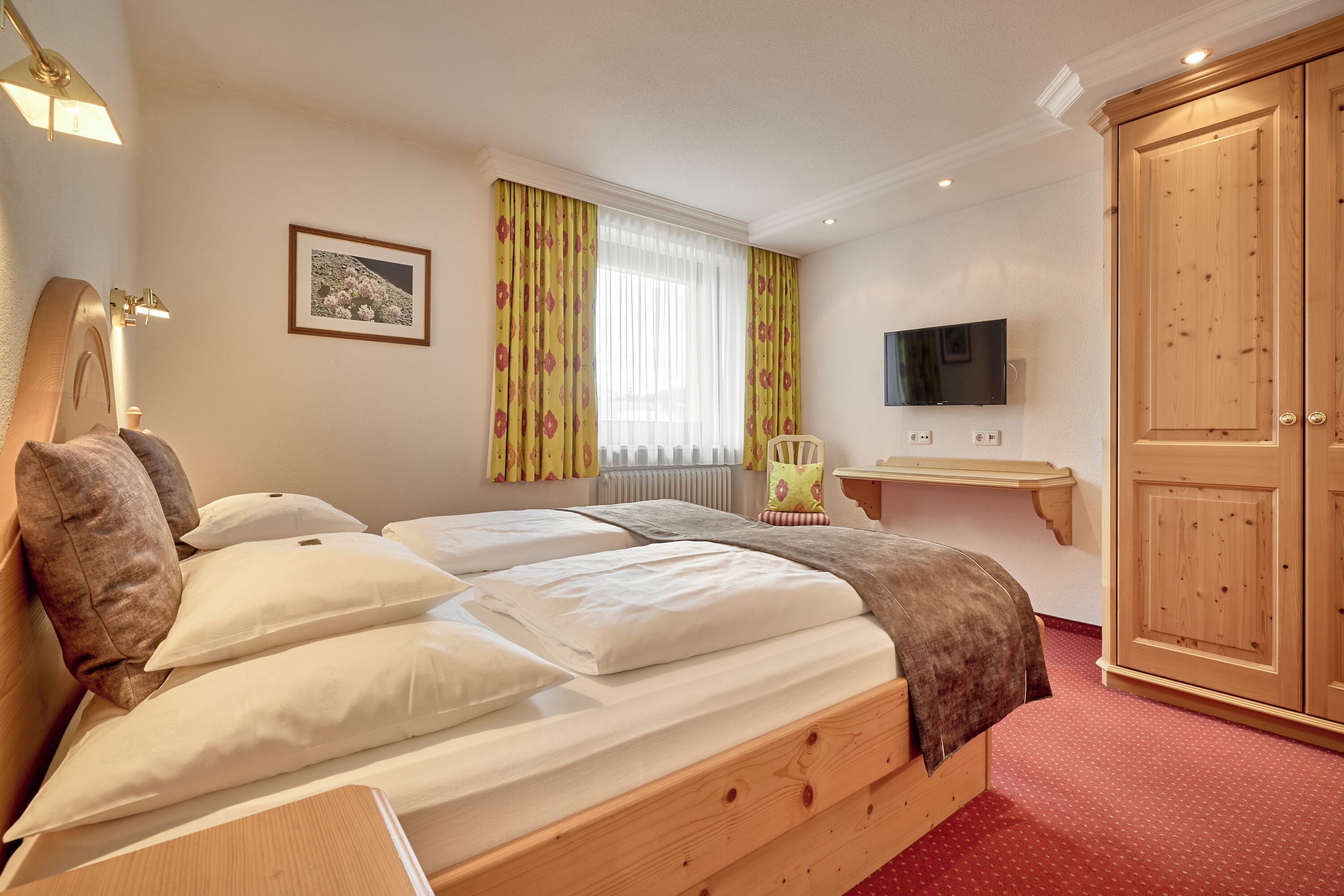 A bedroom with a wooden bed, a bedside table, a TV, and a wardrobe.
