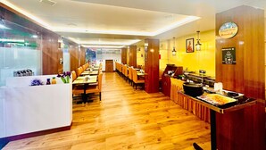Restaurante com piso de madeira, mesas compridas e um buffet com diversos alimentos.